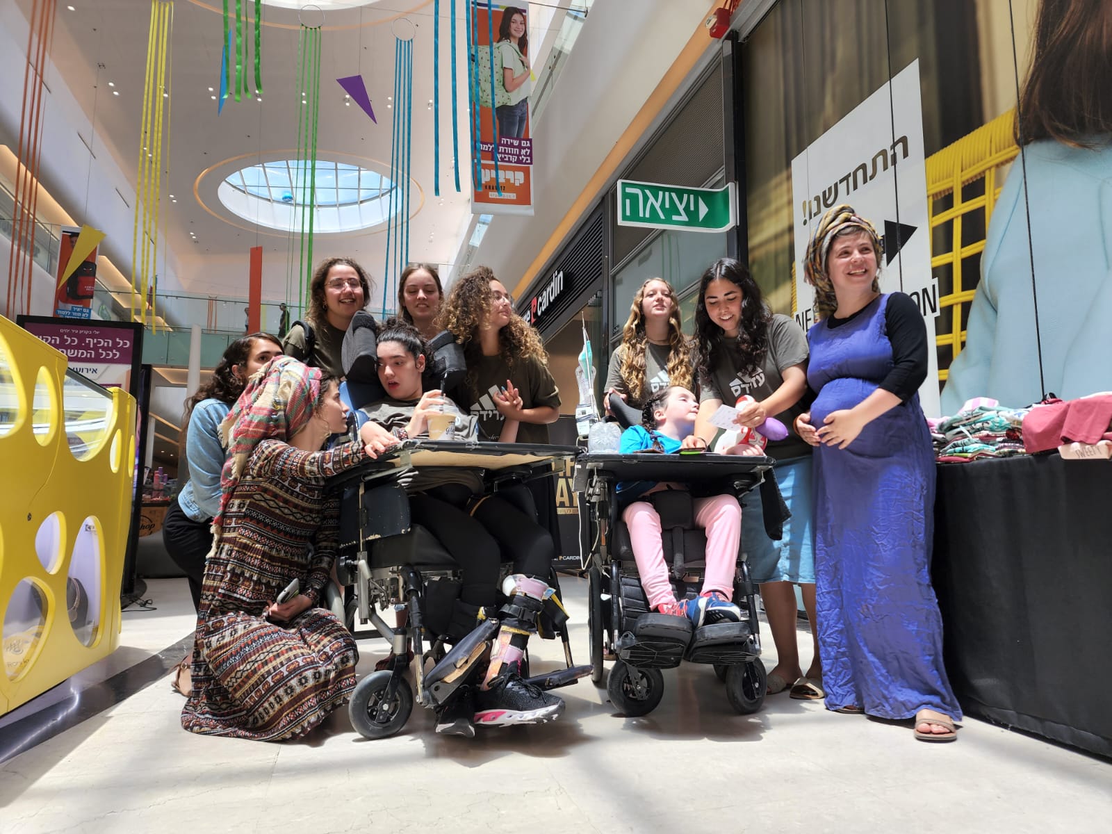 Two gilrs in wheelchairs and counselors in a mall שתי בנות בכסאות גלגלים עם מדריכות בקניון
