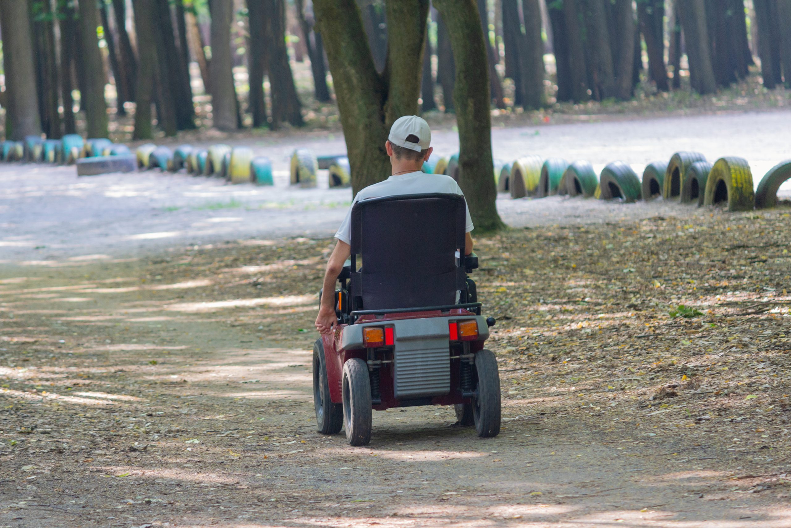 איש בכסא גלגלים חשמלי מטייל ביער Man in motorized wheelchair moving through a park