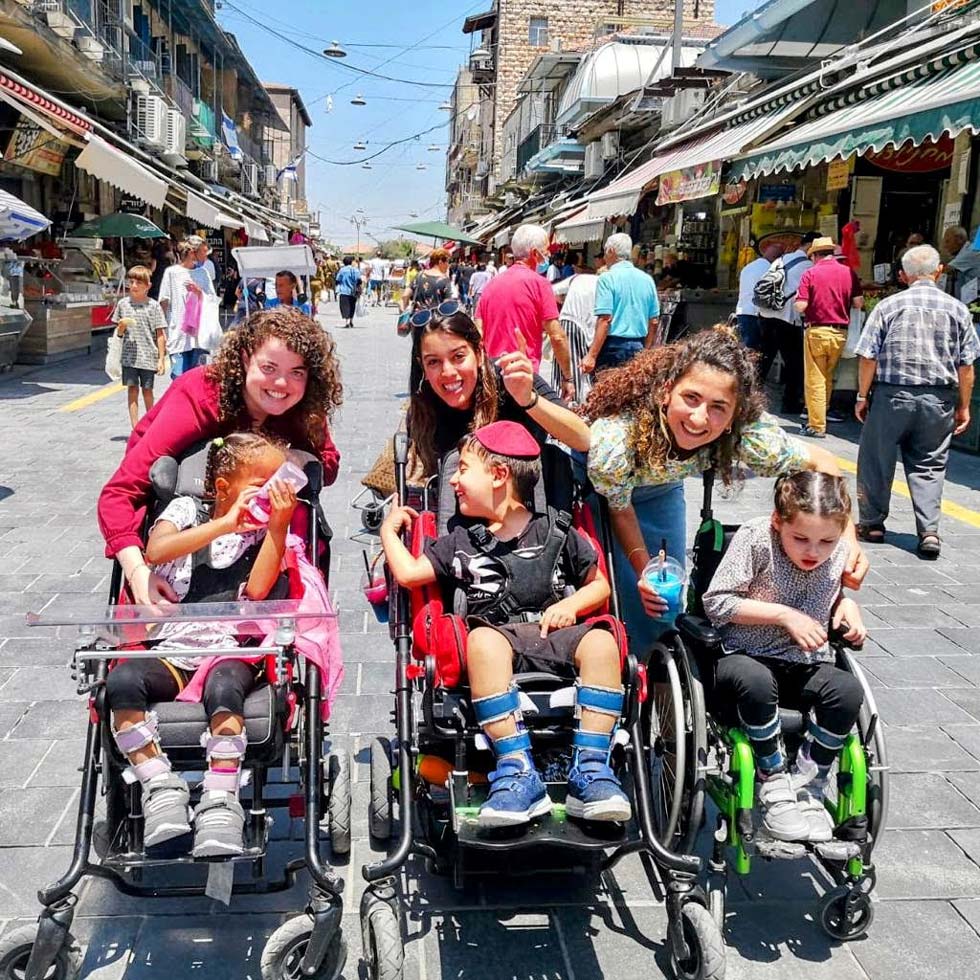 ילדים בכסאות גלגלים ומלווים בשוק Kids in wheelchairs and escorts at open air market