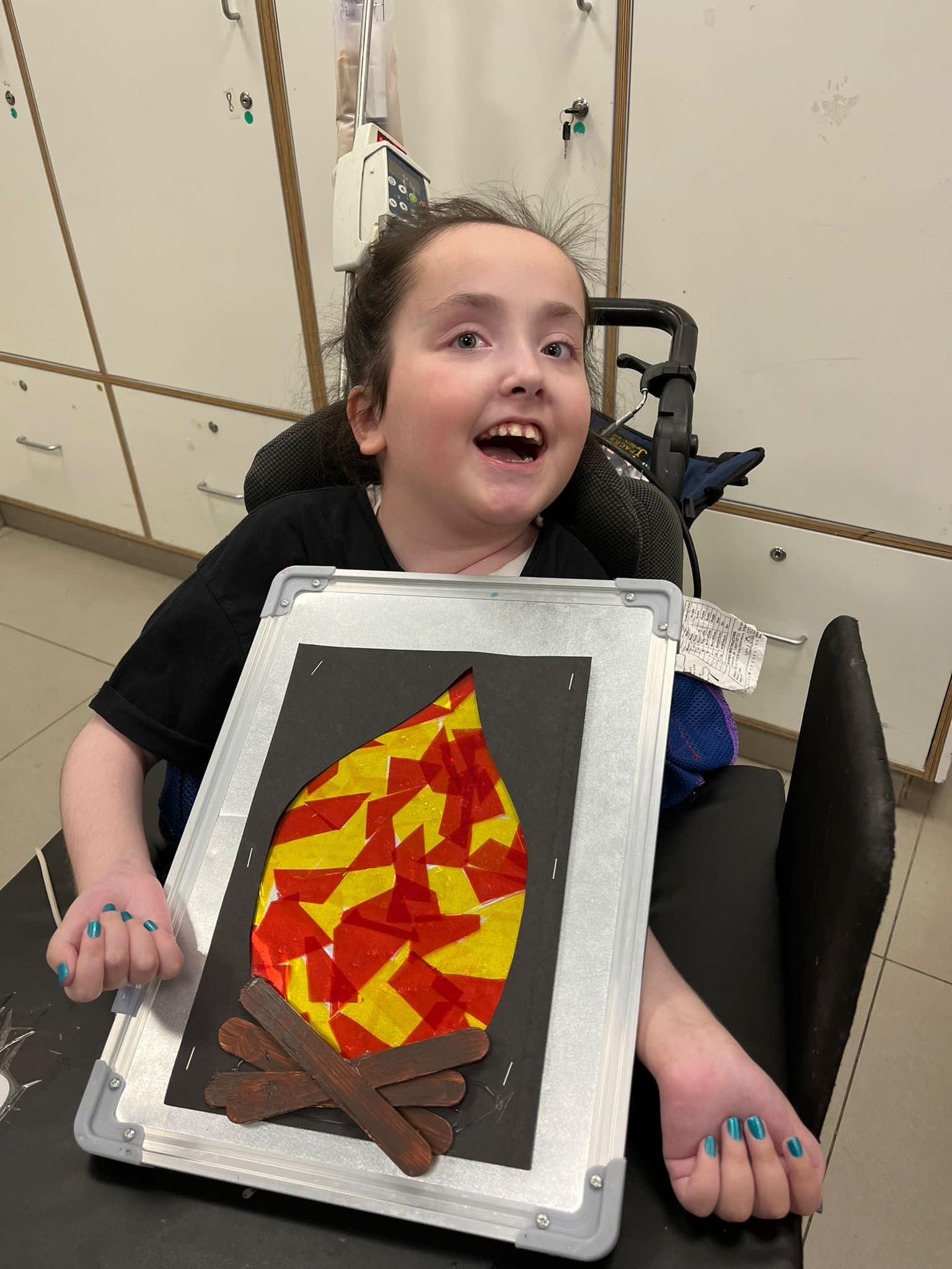 ילדה בכסא גלגלים מחזיקה תמונה של מדורה Girl in a wheelchair holding a picture of a bonfire