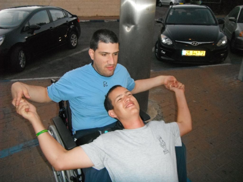 Young man in a wheelchair with a volunteer in a parking lot בחור בכסא גלגלים עם מתנדב בחניון