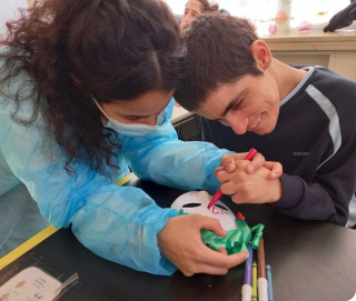 Woman helping a young man with disabilities color a mask אישה עוזרת לבחור עם מגבלויות צובע מסיכה
